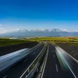 Słowacja: płatne drogi z widokiem na Tatry. Dwie jezdnie autostrady, rozmyte samochody, zielone pola i majestatyczne góry w tle.