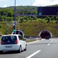 Biały samochód zbliża się do tunelu w Chorwacji. Znak drogowy informuje o opłatach za autostrady.
