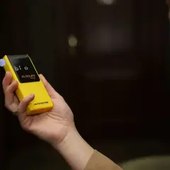 Dłoń trzyma żółty alkomat z wyświetlaczem. Czy w Żabce są alkomaty? Ten model jest limitowaną edycją.