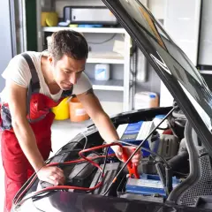 Mechanik podłącza prostownik do akumulatora. Zastanawiasz się, ile kosztuje naładowanie akumulatora u mechanika?
