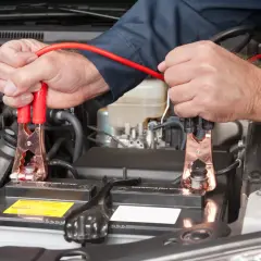 Podłączanie kabli rozruchowych do akumulatora 24v. Mechanik w ciemnej koszuli podłącza czerwone kable do biegunów akumulatora samochodowego.