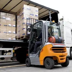 Operator wózka widłowego dba o bezpieczeństwo ładunku, rozładowując palety z kartonami z naczepy ciężarówki.
