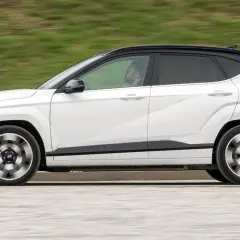 Biały Hyundai Kona w ruchu, z czarnym dachem i przyciemnianymi szybami. Kierowca widoczny w kabinie. Sprawdź hyundai kona wymiary.