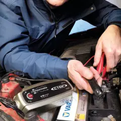 Mężczyzna podłącza prostownik CTEK do akumulatora, by sprawdzić, jak sprawdzić czy prostownik jest dobry.