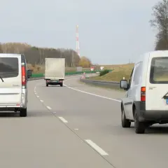 Na autostradzie widać kilka pojazdów, w tym dwa białe busy i jeden tir. Zastanawiasz się, ile tir może jechać na autostradzie?