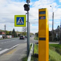 Żółty fotoradar stoi przy drodze z pasami. Z jakiej odległości łapią fotoradary? To pytanie zadaje sobie wielu kierowców.