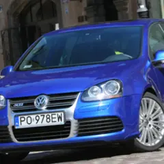Błękitny Golf R32 z felgami ze stopów lekkich, zaparkowany na brukowanej uliczce przed kawiarnią.