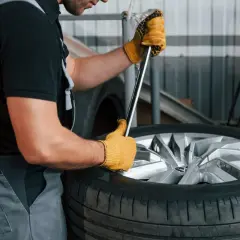 Mechanik w żółtych rękawicach próbuje odkręcić zapieczone koło z piasty za pomocą klucza.