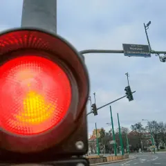 Zbliżenie na czerwone światło sygnalizatora, obok widać rejestrator przejazdu na czerwonym świetle i znak ronda Jana Nowaka-Jeziorańskiego.
