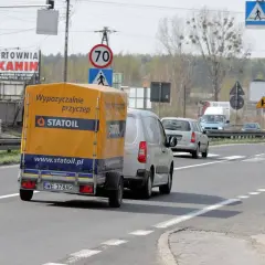 Na drodze widać przyczepę z napisem "Wypożyczalnie przyczep Statoil". Znak ograniczenia prędkości wskazuje 70 km/h, co sugeruje, ile autobus może jechać na autostradzie w takich warunkach.