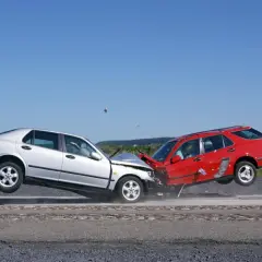 Srebrny i czerwony samochód po zderzeniach czołowych, oba w powietrzu, z widocznymi uszkodzeniami.