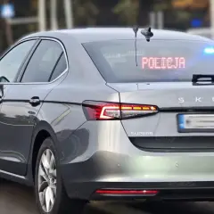 Szary Skoda Superb, jeden z policyjnych samochodów nieoznakowanych, z zapalonym napisem "POLICJA" na tylnej szybie i niebieskimi światłami.