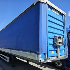Naczepa tira z niebieską plandeką, gotowa do trasy. Standardowa ile szerokości ma naczepa tira, by pomieścić ładunek.