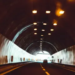 Samochód jedzie przez tunel, pokonując kolejne odległości w tunelu. Światła sufitowe oświetlają drogę.