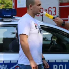 Policjant bada alkomatem mężczyznę stojącego obok radiowozu.