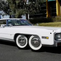 Biały Cadillac Eldorado z podwójnymi kołami z przodu i z tyłu. Ten niezwykły samochód ma aż cztery osie, co czyni go wyjątkowym na drodze.