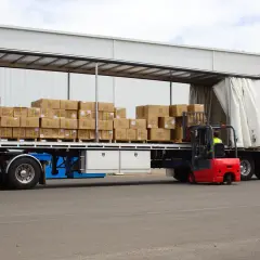Czerwony wózek widłowy ładuje pudła na naczepę. Taki tir może przewieźć nawet 25 ton ładunku.