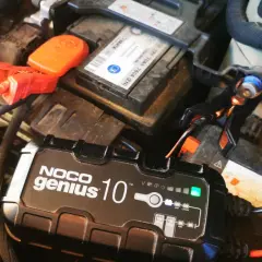 Prostownik NOCO Genius 10 ładuje akumulator samochodowy. Zielona lampka wskazuje, że ładowanie przebiega prawidłowo. Gwiazdka na prostowniku oznacza tryb pracy.