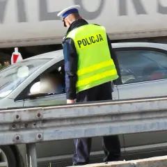 Policjant w kamizelce odblaskowej kontroluje kierowcę. Pamiętaj, że za brak pasów grożą punkty karne.