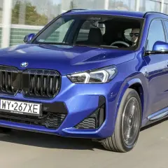 Niebieskie BMW X1 w ruchu drogowym, widok z przodu.