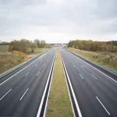 Pusta autostrada w Niemczech, gdzie podróżowanie jest bezpłatne. W oddali widać budynki i jesienne drzewa.