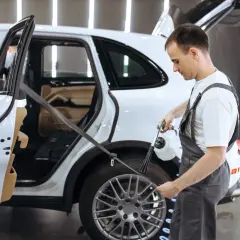 Mężczyzna w warsztacie samochodowym pokazuje, jak wyczyścić pasy bezpieczeństwa w białym aucie, używając specjalnego urządzenia.
