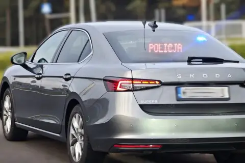 Szary Skoda Superb, jeden z policyjnych samochodów nieoznakowanych, z zapalonym napisem "POLICJA" na tylnej szybie i niebieskimi światłami.