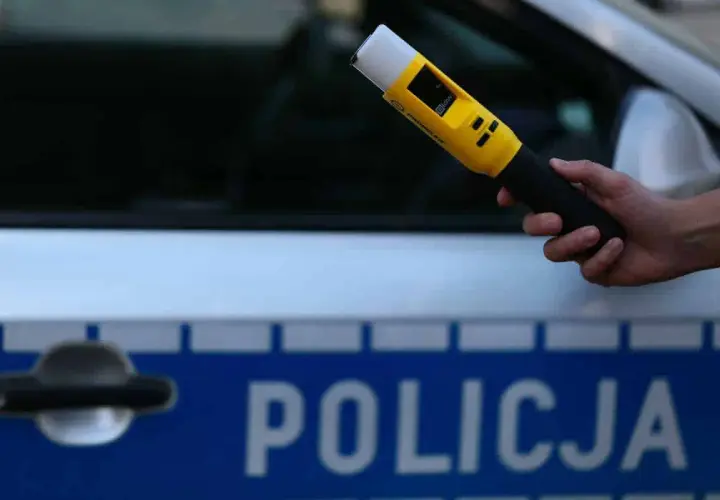 Dłoń trzyma żółty alkomat na tle radiowozu z napisem POLICJA. Czy mogę odmówić dmuchania w alkomat?