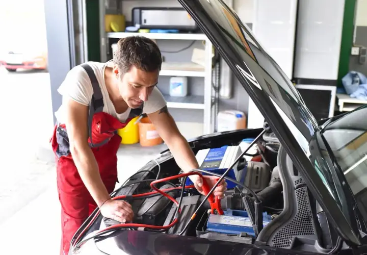Mechanik podłącza prostownik do akumulatora. Zastanawiasz się, ile kosztuje naładowanie akumulatora u mechanika?