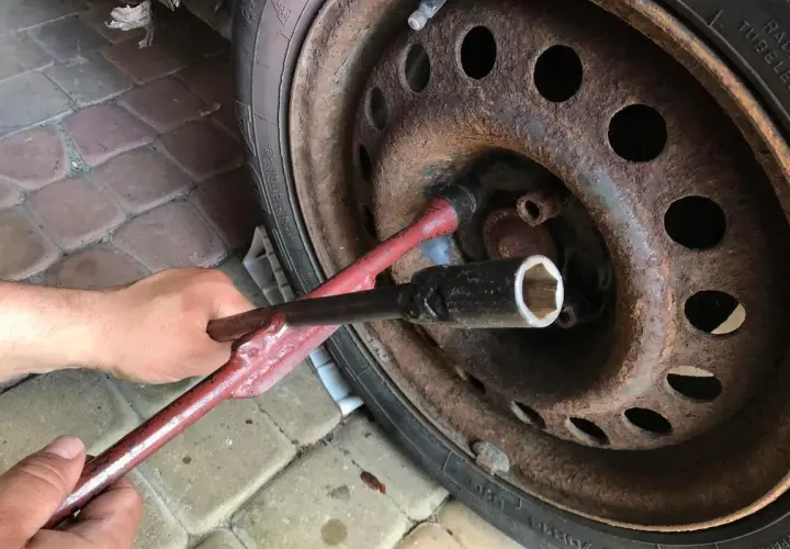 Ręka używa klucza do odkręcenia zapieczonego koła. Rdza na feldze sugeruje, że może to być trudne zadanie.