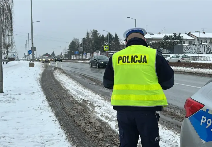 Policjant w kamizelce odblaskowej stoi przy drodze, gdzie kiedy zabierają prawko za prędkość. Śnieg i błoto na poboczu.