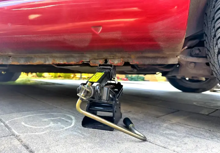 Podnośnik samochodowy pod czerwonym autem, gotowy do akcji. Dowiedz się, jak podnieść auto lewarkiem, by wymienić koło.