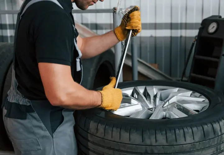 Mechanik w żółtych rękawicach próbuje odkręcić zapieczone koło z piasty za pomocą klucza.