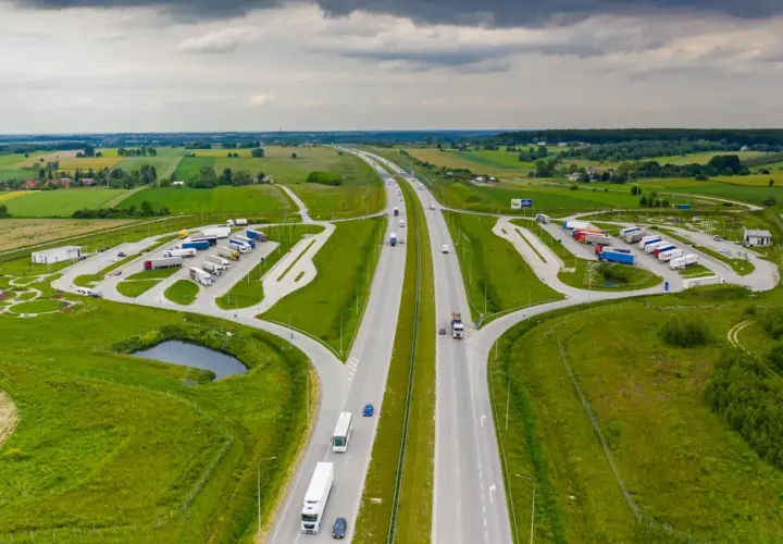 Miejsce obsługi podróżnych (MOP) na autostradzie, z parkingiem dla ciężarówek i samochodów osobowych, otoczone zielenią.