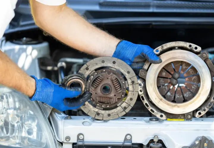 Mechanik w niebieskich rękawiczkach pokazuje zużyte części sprzęgła. Zastanawiasz się, ile kosztuje wymiana sprzęgła?