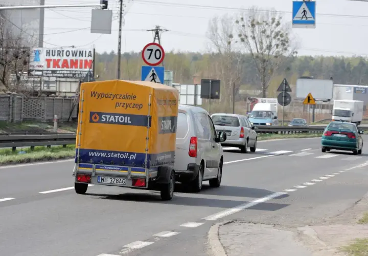 Na drodze widać przyczepę z napisem "Wypożyczalnie przyczep Statoil". Znak ograniczenia prędkości wskazuje 70 km/h, co sugeruje, ile autobus może jechać na autostradzie w takich warunkach.