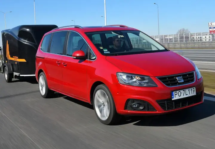 Czerwony Seat Alhambra z przyczepą na autostradzie. Zastanawiasz się, ile możesz jechać z przyczepą na autostradzie?