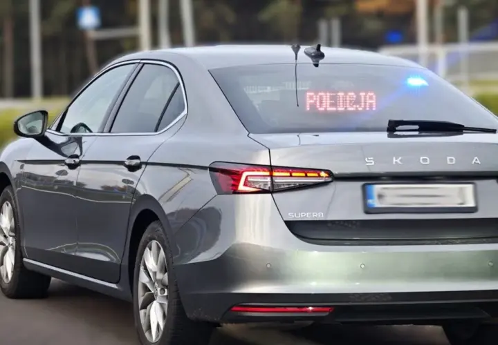 Szary Skoda Superb, jeden z policyjnych samochodów nieoznakowanych, z zapalonym napisem "POLICJA" na tylnej szybie i niebieskimi światłami.