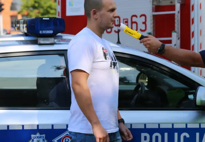Policjant bada alkomatem mężczyznę stojącego obok radiowozu.
