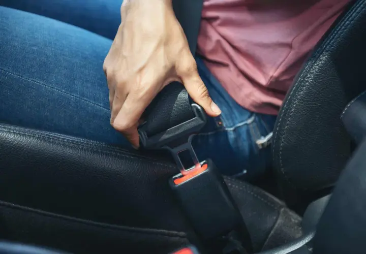 Dłoń próbuje odpiąć pas bezpieczeństwa w samochodzie. Dowiedz się, jak naprawić zablokowany pas bezpieczeństwa, gdy mechanizm nie działa.
