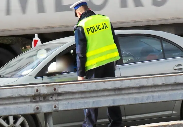 Policjant w kamizelce odblaskowej kontroluje kierowcę. Pamiętaj, że za brak pasów grożą punkty karne.