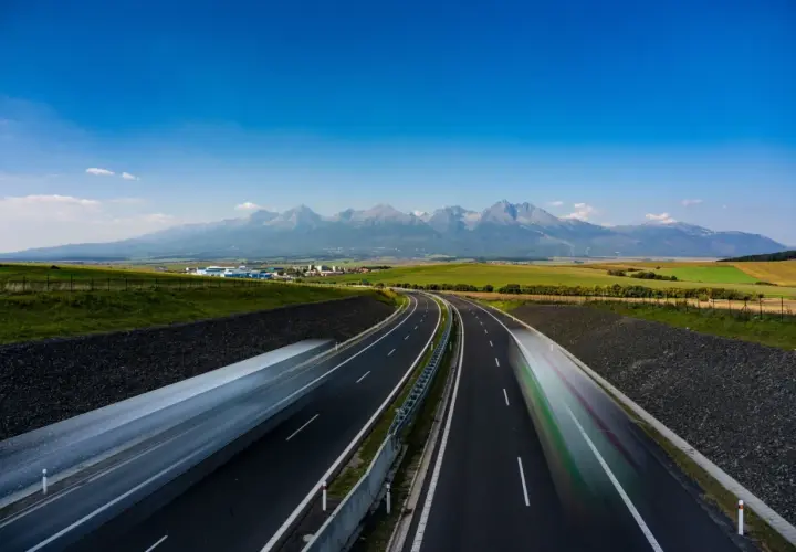 Słowacja: płatne drogi z widokiem na Tatry. Dwie jezdnie autostrady, rozmyte samochody, zielone pola i majestatyczne góry w tle.