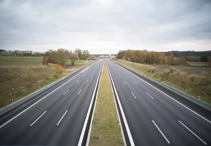 Pusta autostrada w Niemczech, gdzie podróżowanie jest bezpłatne. W oddali widać budynki i jesienne drzewa.