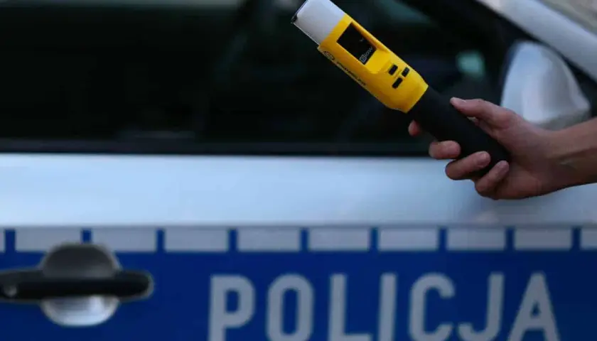 Dłoń trzyma żółty alkomat na tle radiowozu z napisem POLICJA. Czy mogę odmówić dmuchania w alkomat?