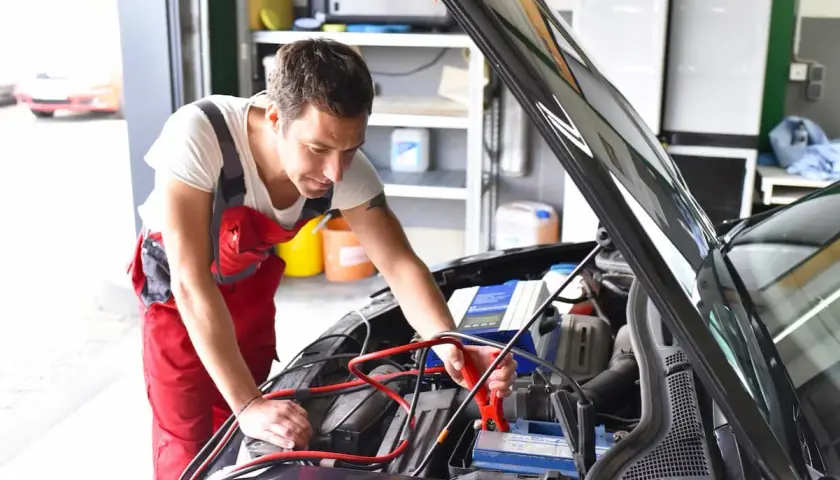 Mechanik podłącza prostownik do akumulatora. Zastanawiasz się, ile kosztuje naładowanie akumulatora u mechanika?