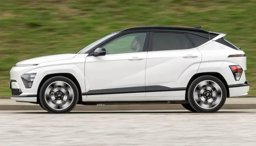 Biały Hyundai Kona w ruchu, z czarnym dachem i przyciemnianymi szybami. Kierowca widoczny w kabinie. Sprawdź hyundai kona wymiary.