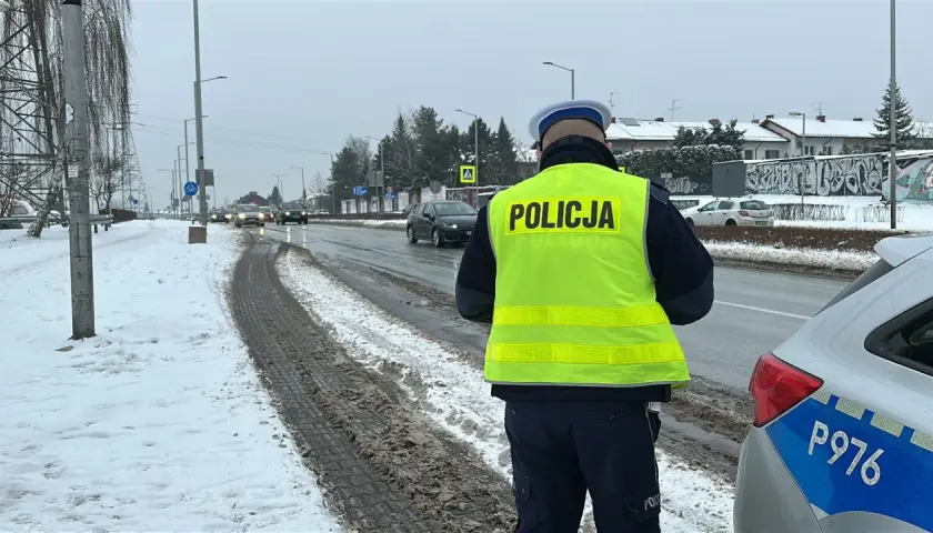 Policjant w kamizelce odblaskowej stoi przy drodze, gdzie kiedy zabierają prawko za prędkość. Śnieg i błoto na poboczu.