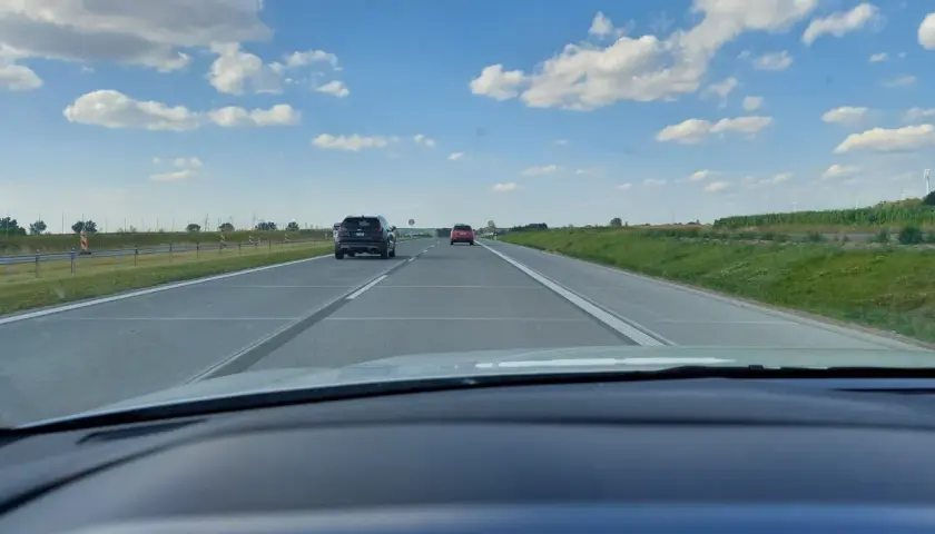 Widok z samochodu na autostradzie. Widać inne pojazdy i znaki ograniczające prędkość do 80 km/h.