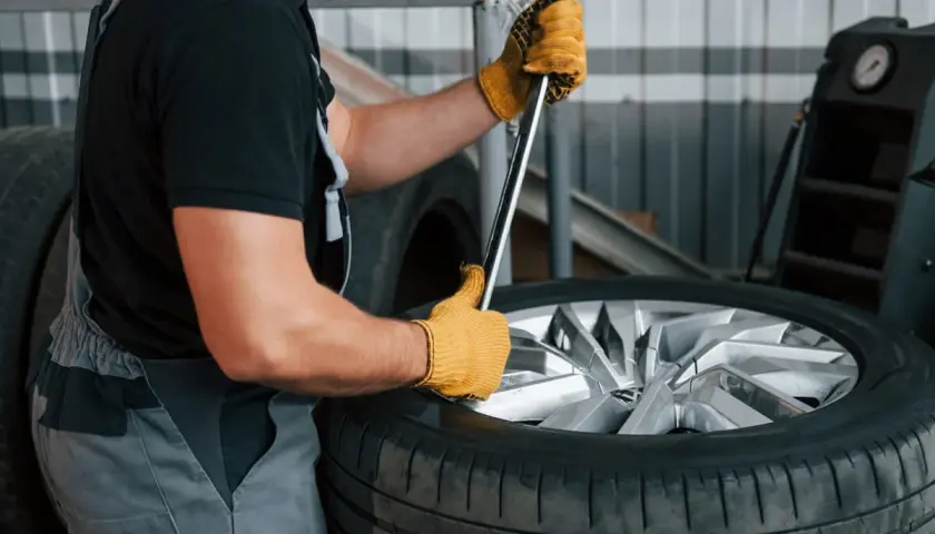 Mechanik w żółtych rękawicach próbuje odkręcić zapieczone koło z piasty za pomocą klucza.