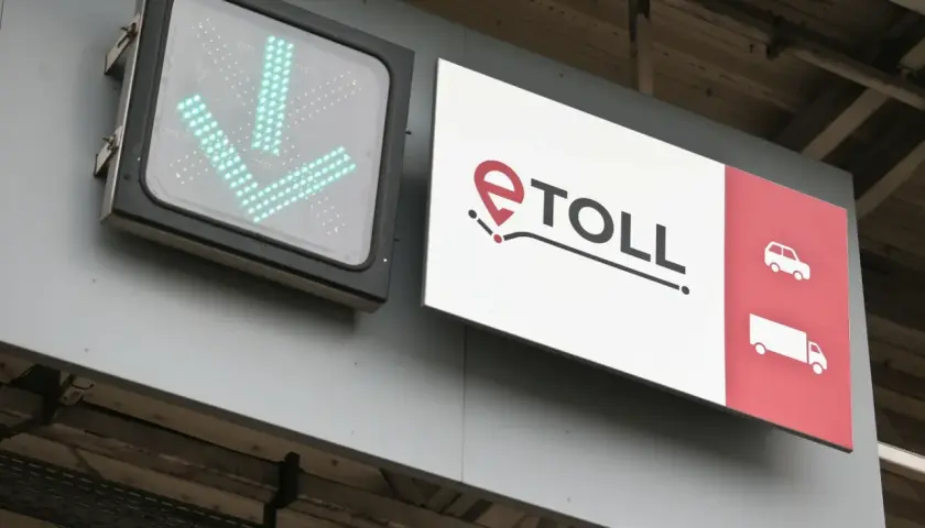 Zielony znak ze strzałkami w dół i logo e-TOLL. Informuje, jak zapłacić za autostradę, wskazując drogę dla samochodów i ciężarówek.